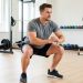 Un homme adulte débutant réalise un squat au poids du corps avec une posture contrôlée dans une salle de fitness lumineuse.