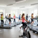 Salle de fitness moderne et lumineuse en France, avec des femmes et des hommes pratiquant la musculation et le cardio-training sur différents appareils.
