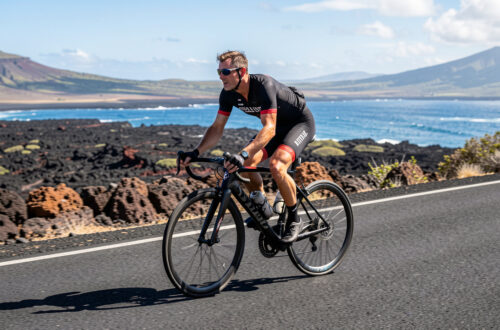 Triathlète amateur à vélo sur une route volcanique d’Hawaï, exposé à la chaleur et au vent latéral sous une lumière naturelle réaliste.
