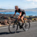 Triathlète amateur à vélo sur une route volcanique d’Hawaï, exposé à la chaleur et au vent latéral sous une lumière naturelle réaliste.